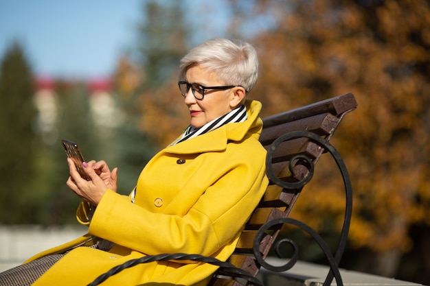 femme âgée est assise sur un banc avec un téléphone