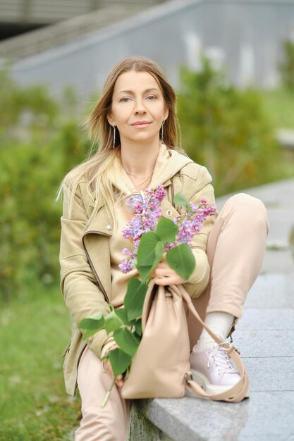 Une femme âgée est assise à l'embarquement avec une branche de lilas dans ses mains