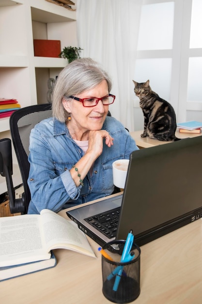 Femme âgée étudiant devant un ordinateur avec son chat