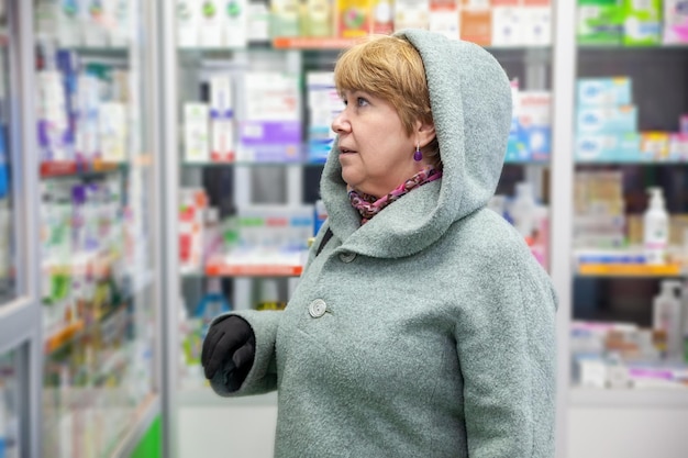 Une femme âgée étudie une vitrine en pharmacie et choisit des vitamines au printemps