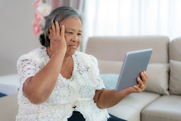 Femme âgée faisant appel vidéo avec son médecin avec ses maux de tête sur tablette numérique consultation en ligne de services de technologie numérique de soins de santé tout en restant à la maison.