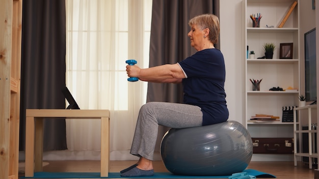 Femme âgée faisant de l'exercice avec des haltères en regardant une leçon en ligne sur une tablette. Formation en ligne technologie d'apprentissage vieille femme formation de levage mode de vie sain sport fitness entraînement à la maison avec nous