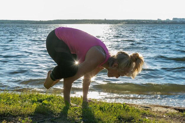 Une femme âgée fait du sport à l'aube sur la rive du lac Une femme fait des poses de yoga Déviation du corps Sports de plein air