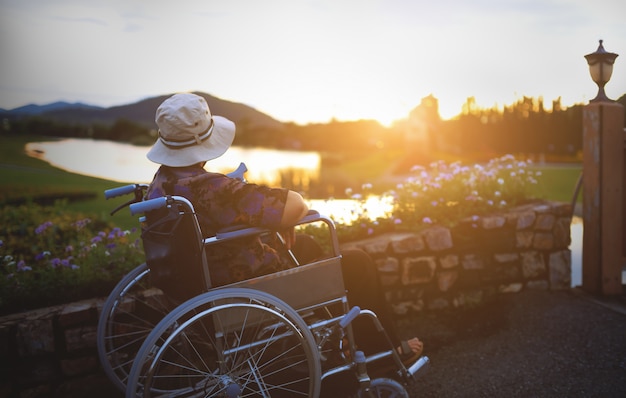 Photo femme âgée sur fauteuil roulant dans le jardin en regardant le coucher du soleil.