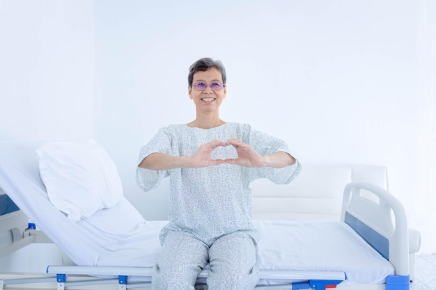 Femme âgée formant un cœur avec ses mains tout en étant soignée à l'hôpital Concept d'assurance maladie pour soins médicaux