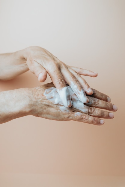 Femme âgée frottant la crème pour les mains, gros plan, espace de copie de fond pastel minimal, concept de soins personnels