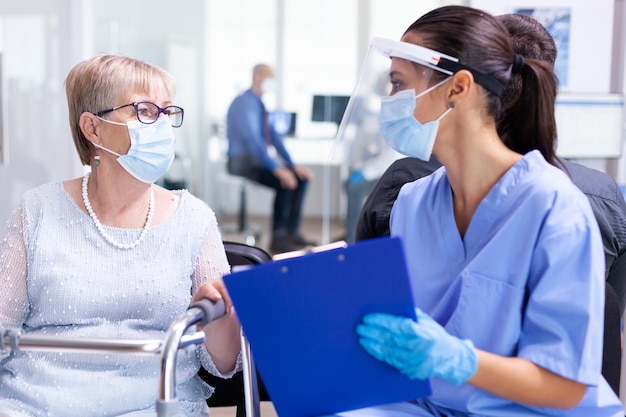 Femme âgée handicapée avec déambulateur discutant avec un médecin spécialiste dans la salle d'attente de l'hôpital