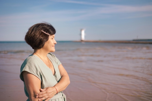 Une femme âgée heureuse en longue robe se promène sur la plage d'une île tropicale au coucher du soleil d'été