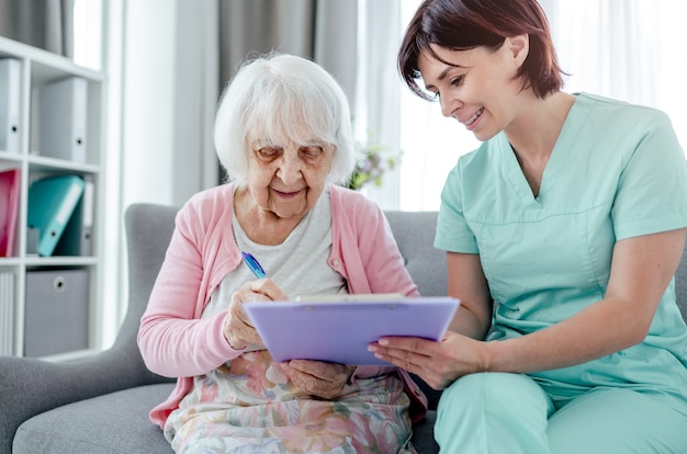 Une femme âgée et une infirmière signent des documents à la maison. Une travailleuse de la santé se soucie de la personne âgée à l'intérieur
