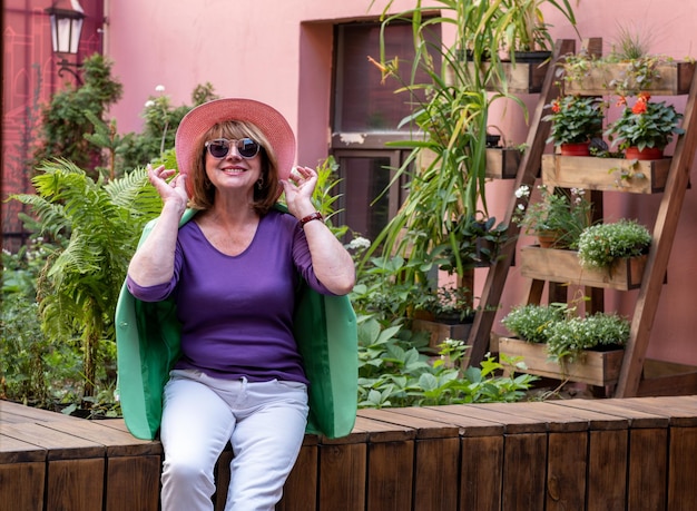 Femme âgée joyeuse portant des lunettes de soleil à la mode et un chapeau sur fond floral et riant