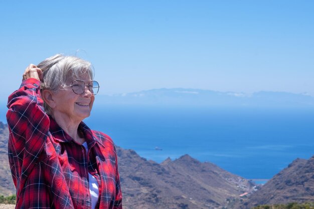 Femme âgée joyeuse profitant des vacances exprimant la joie et la liberté en arrière-plan les montagnes de Tenerife et l'océan atlantique