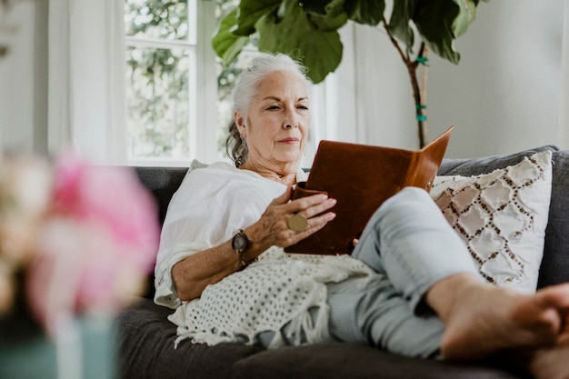 Femme âgée lisant un livre sur un canapé en un week-end