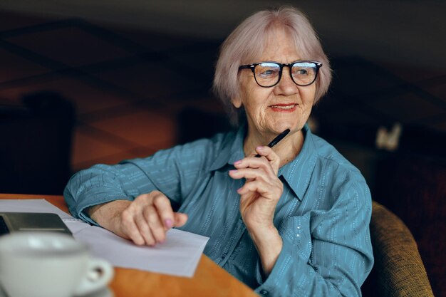 Une femme âgée avec des lunettes est assise à une table devant un ordinateur portable inchangé