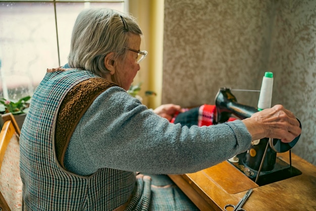 Femme âgée à lunettes utiliser une machine à coudre mains ridées de la vieille couturière femme âgée Vieille machine à coudre Machine à coudre manuelle de style rétro classique prête pour le travail de couture