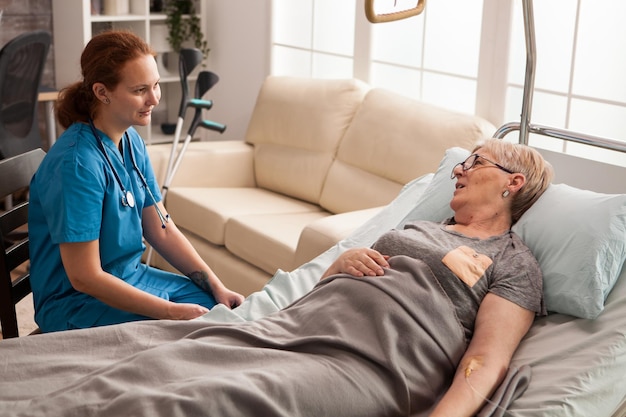 Femme âgée malade allongée sur son lit dans une maison de retraite parlant avec une infirmière.