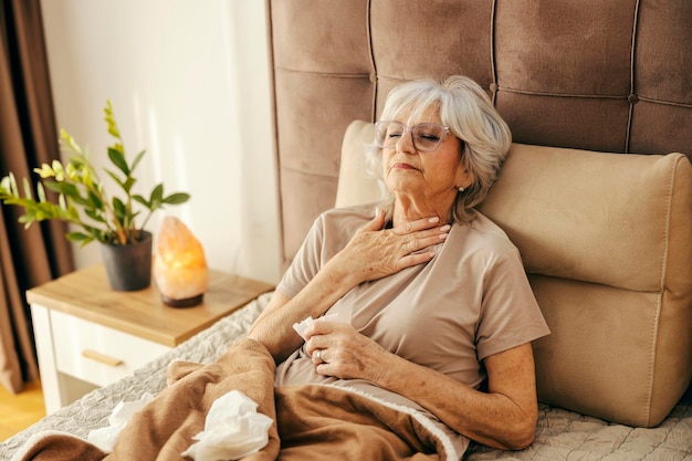 Une femme âgée malade avec la grippe est allongée au lit et a une laryngite