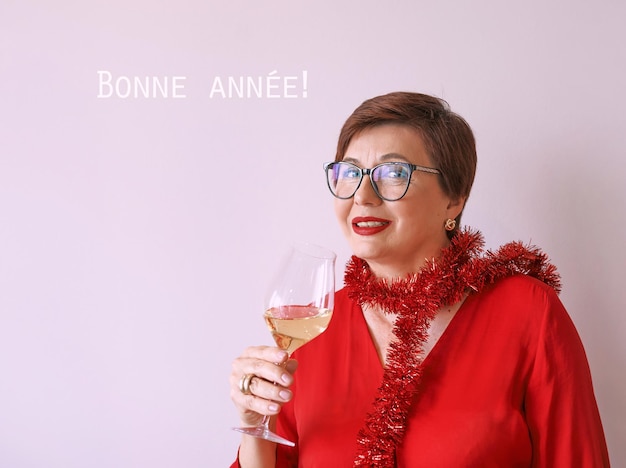 femme âgée mature et élégante en chemisier rouge avec un verre de vin blanc célébrant la fête amusante du nouvel an