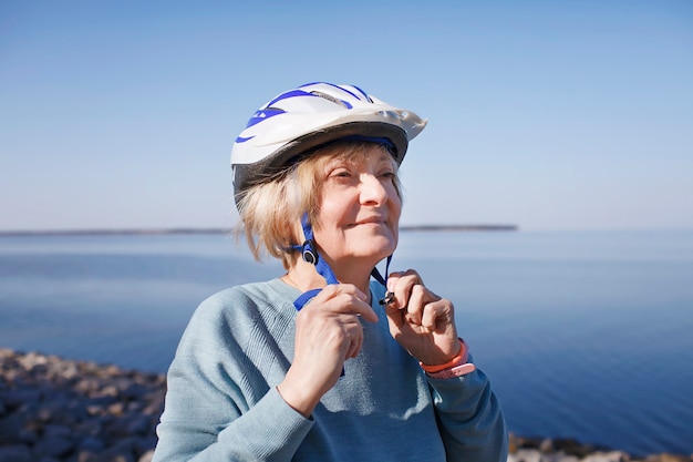 Une femme âgée met un casque de sécurité avant de faire du patin à roulettes dans la nature, la santé mentale et physique