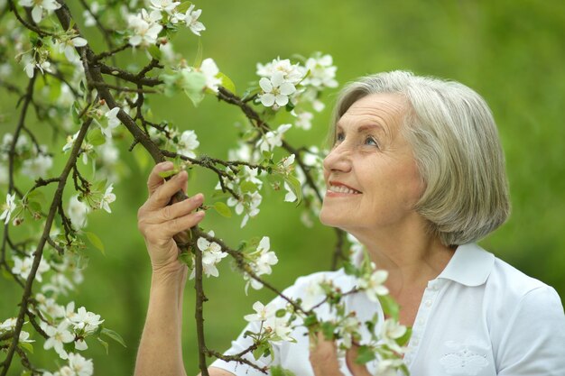 Femme âgée pensive marchant dans la nature printanière avec des fleurs de cerisier