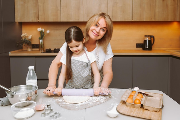 Une femme âgée et une petite fille déroulent de la pâte molle pendant la cuisson dans la cuisine à la maison grand-mère et petite-fille cuisinent des gâteaux