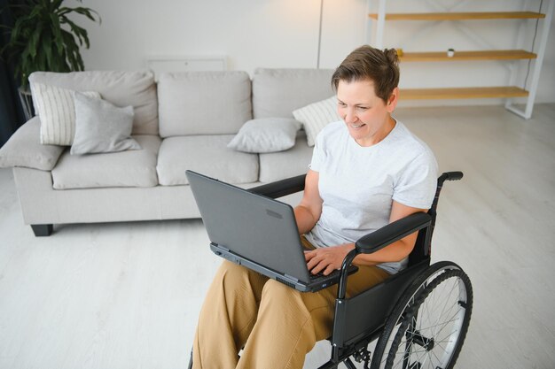 Femme âgée positive en fauteuil roulant travaillant sur ordinateur portable IT pigiste en ligne