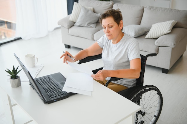 Femme âgée positive en fauteuil roulant travaillant sur ordinateur portable IT pigiste en ligne