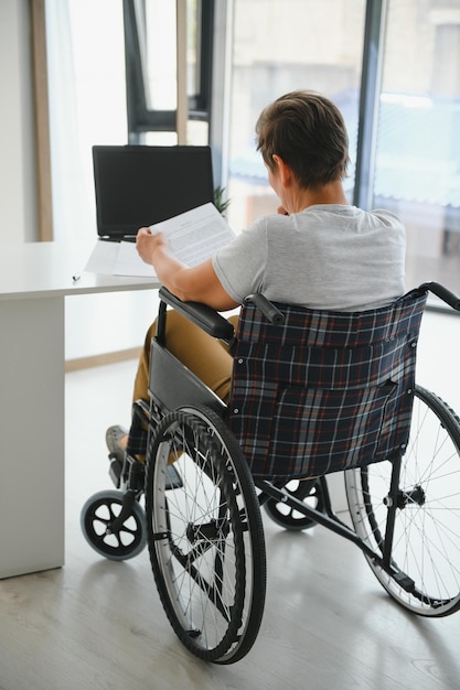 Femme âgée positive en fauteuil roulant travaillant sur ordinateur portable IT pigiste en ligne