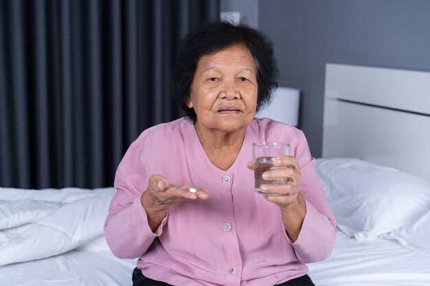 femme âgée prenant la pilule avec un verre d&#39;eau dans un lit