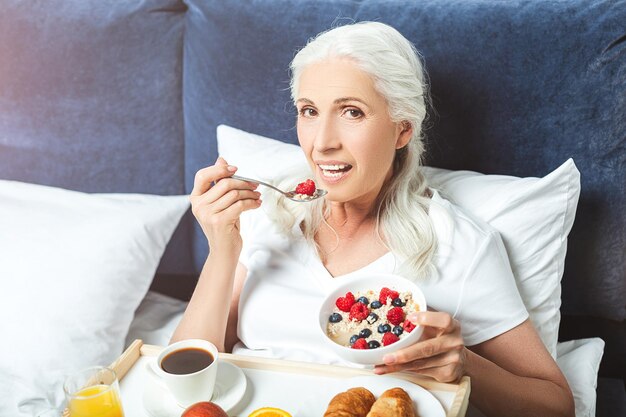 Femme âgée prenant son petit déjeuner au lit et regardant la caméra