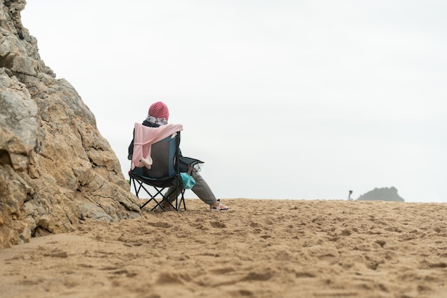 Femme âgée réfléchie assise sur une chaise touristique sur la plage de la mer à la recherche d'horizon Concept de solitude et de vieillesse