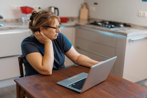 Femme âgée à la retraite frustrée assise sur un canapé à la maison à l'aide d'un ordinateur portable