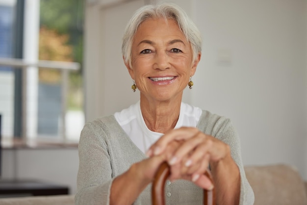 Femme âgée à la retraite se relaxant à la maison Heureuse vieille femme souriante tenant une canne et regardant la caméra avec positivité Grand-mère insouciante et mature assise sur une chaise dans une maison de retraite