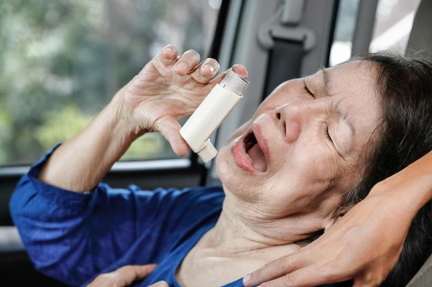 Femme âgée s'étouffant et tenant un spray contre l'asthme à l'intérieur de la voiture sur le chemin