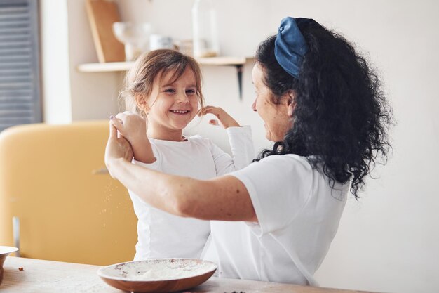 Femme âgée avec sa petite-fille préparant des aliments avec de la farine dans la cuisine