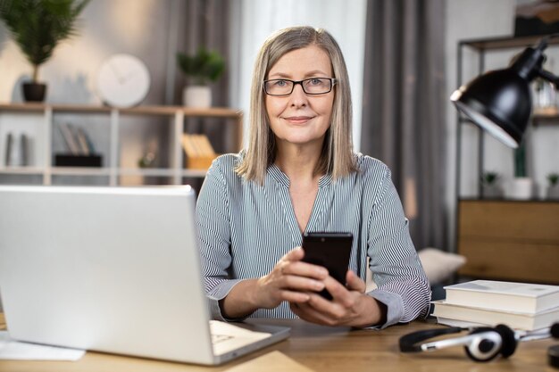 Femme âgée scannant l'écran du téléphone portable à l'intérieur de la maison