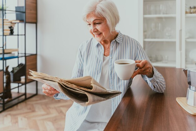 Femme âgée se relaxant à la maison, lisant le journal et prenant son petit-déjeuner