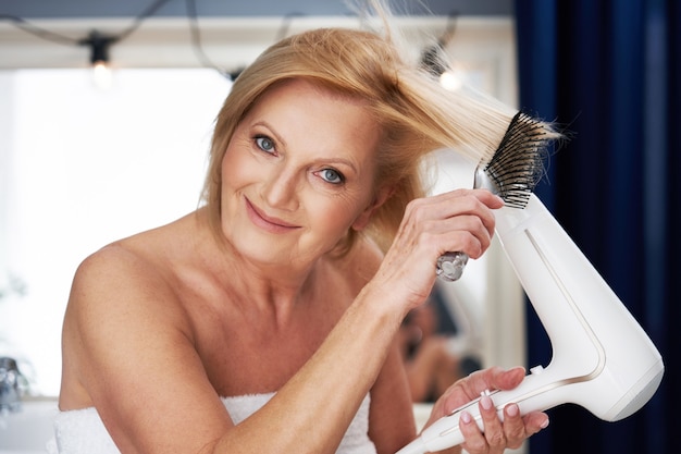 femme âgée, sécher les cheveux dans la salle de bain