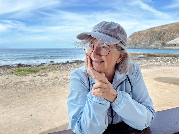 Une femme âgée et séduisante aux cheveux gris sur la plage qui détourne le regard jouit de la liberté et de la retraite.