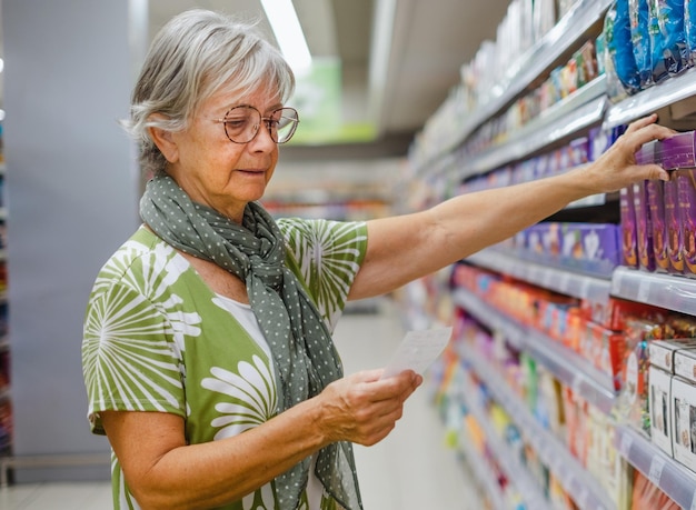Femme âgée sélectionnant des articles d'épicerie dans une rangée du concept de supermarché de l'inflation des prix de consommation