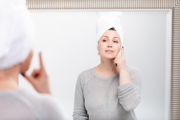 Femme âgée souriante, appliquer une crème anti-âge