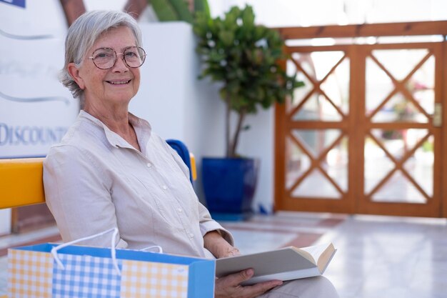 Femme âgée souriante assise à l'extérieur sur un banc jaune tout en lisant un livre jolie dame à la retraite avec des lunettes appréciant lire et apprendre