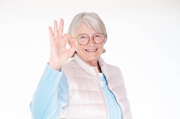 Femme âgée souriante aux cheveux blancs regardant la caméra montrant le signe ok