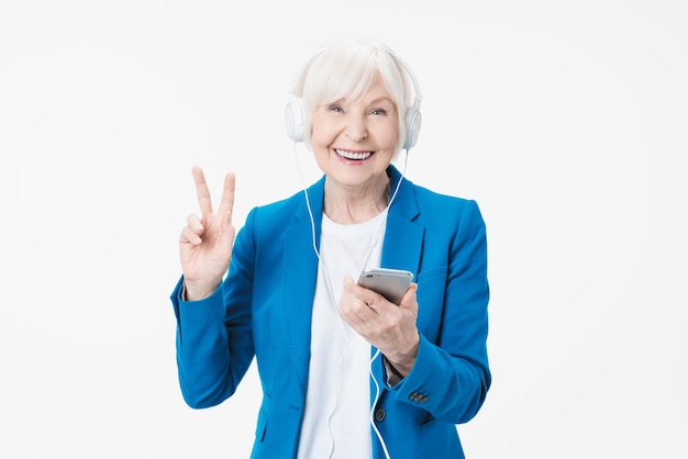 Femme âgée souriante avec un casque écoutant de la musique sur téléphone isolé sur fond blanc