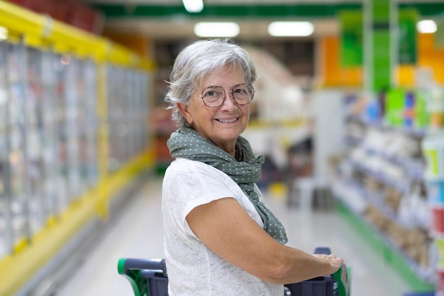 Femme âgée souriante avec chariot achetant de la nourriture au supermarché