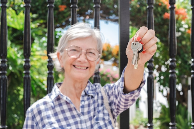 Femme âgée souriante défocalisée tenant les clés de la maison achat immobilier concept de location