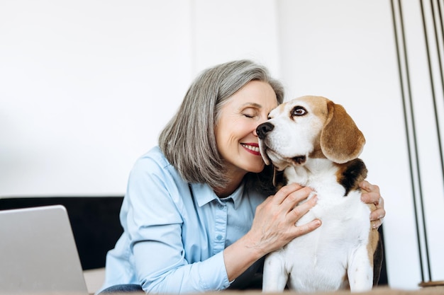 Une femme âgée souriante embrassant un chien beagle à la maison