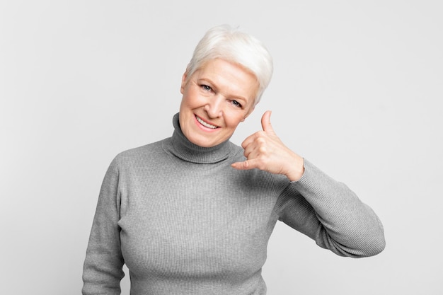 Une femme âgée souriante fait des gestes. Appelez-moi.