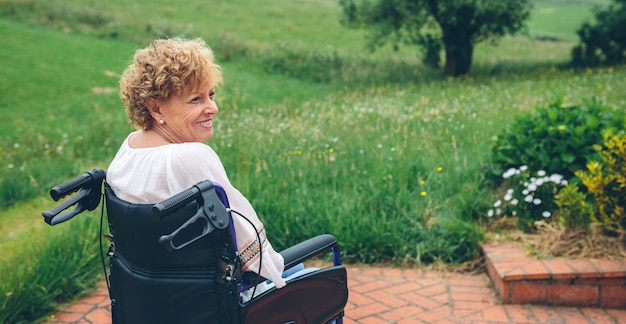 Femme âgée souriante en fauteuil roulant dans le jardin