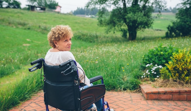 Femme âgée souriante en fauteuil roulant dans le jardin