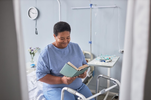 Femme âgée souriante lisant un livre dans une chambre d'hôpital